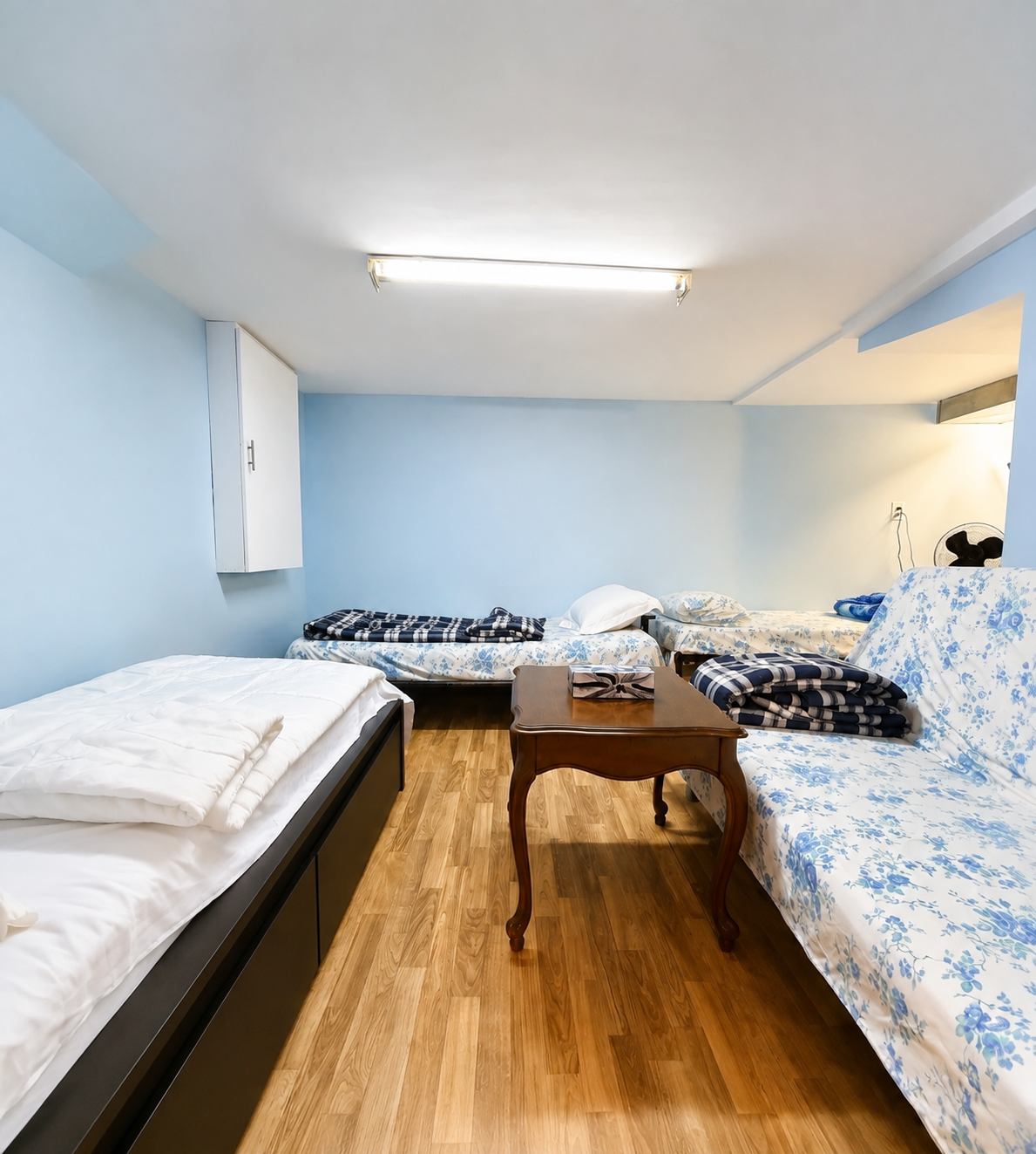 Wide view of shared accommodation room with multiple beds, fresh linens, seating area, and open floor space for SonoRAY course participants